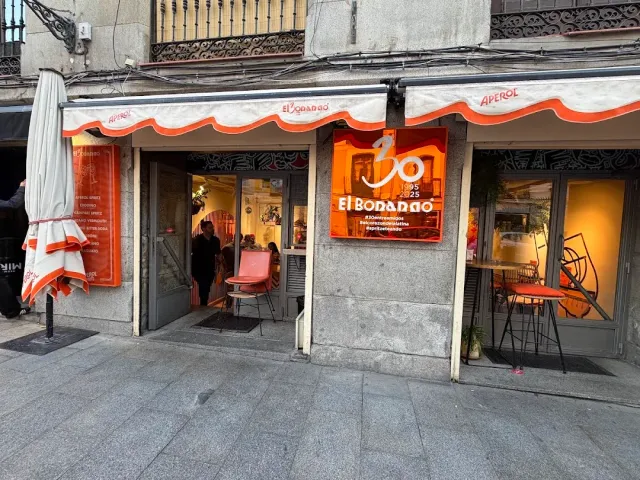 An orange and white frontage with a wavy awning, a lit sign and chairs outside