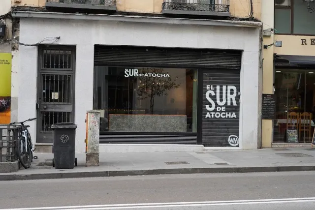 A closed black shopfront with large white lettering, a rubbish bin and a bicycle on the pavement