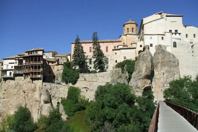 Houses with wooden balconies hanging over the edge of a rock cliff, with a large stone building behind