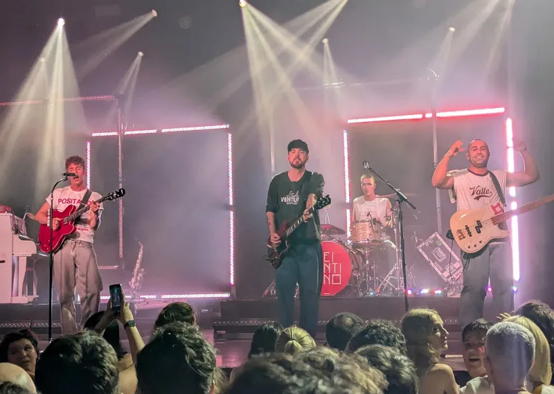 A band playing on a stage lit purple and red with a packed crowd in front of it