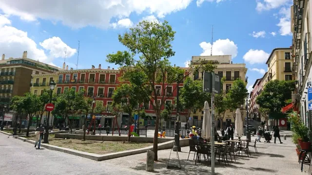 An open square with young trees, terrace tables and red residential buildings behind
