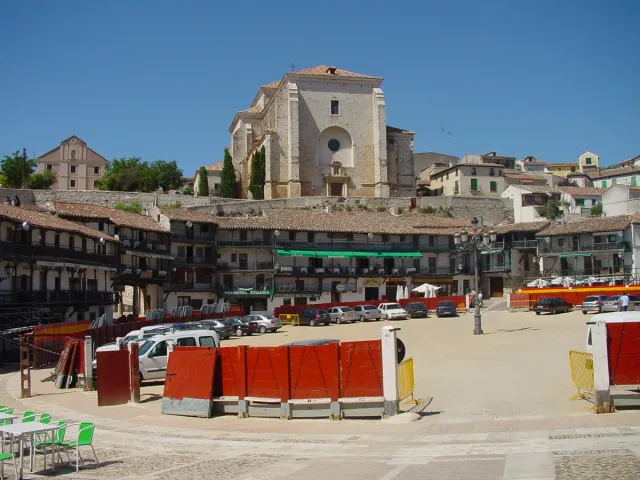 A round square lined with houses with green wooden balconies and a stone church on the hill above