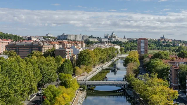 A high view over a narrow river and its bridges, tree lined avenues and a skyline with a palace and a cathedral