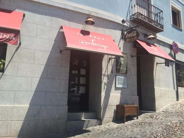 A gray stone facade with red awnings on a cobbled street