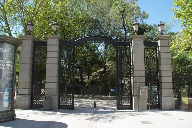 A wide black iron gate between stone pillars at the entrance to a shaded park