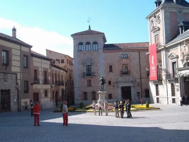 A small paved square ringed by old brick and stone buildings, with a tower and a statue at its centre
