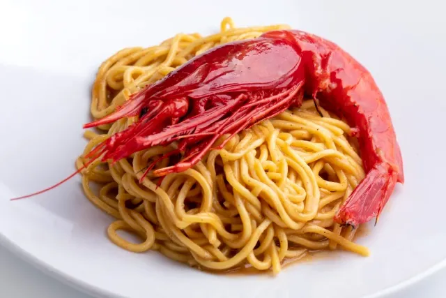 A plate of spaghetti with a large red prawn laid on top