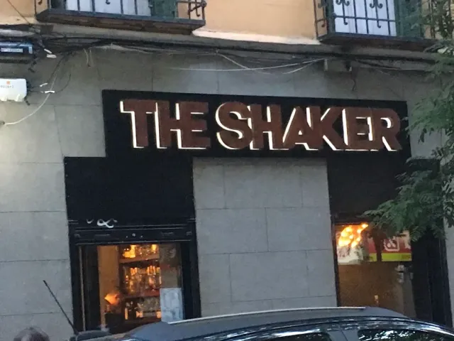 A lit letter sign on a gray stone frontage above a display window in the evening