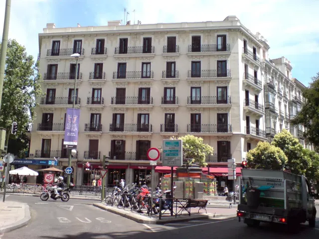 A corner cafe in a pale stone building with an awning and large windows facing a busy street
