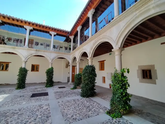 An inner courtyard with stone arches, columns, green climbing plants and a wooden upper gallery
