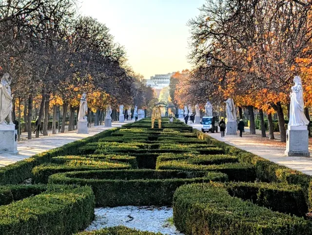 An avenue with clipped hedges in a pattern, and white stone statues along both sides