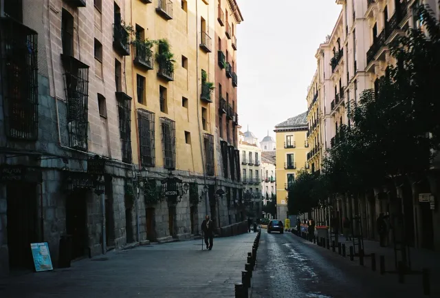 A narrow street between tall houses with iron balconies and stone arches housing restaurants