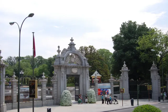 An ornate stone gate with columns and a carved crest at a park entrance framed by trees