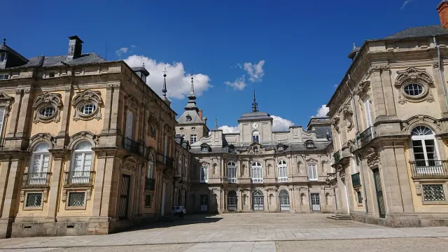 A Baroque palace courtyard in pale stone with a clock tower and domes under a blue sky