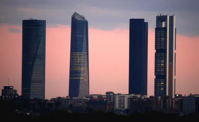 Four glass skyscrapers of differing heights at the edge of the city against a pink sunset sky