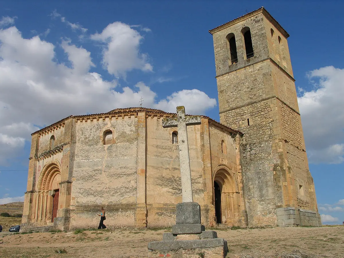 A polygonal romanesque stone church with a bell tower standing in open country under a blue sky