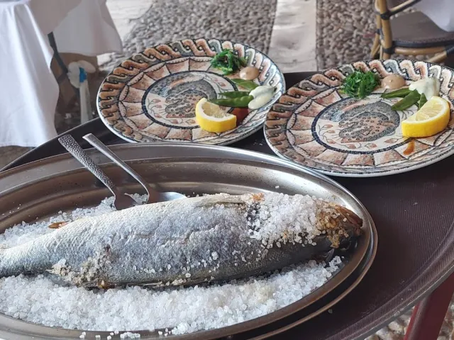 A whole fish baked in coarse salt on a metal tray, and beside it two decorated plates with lemon