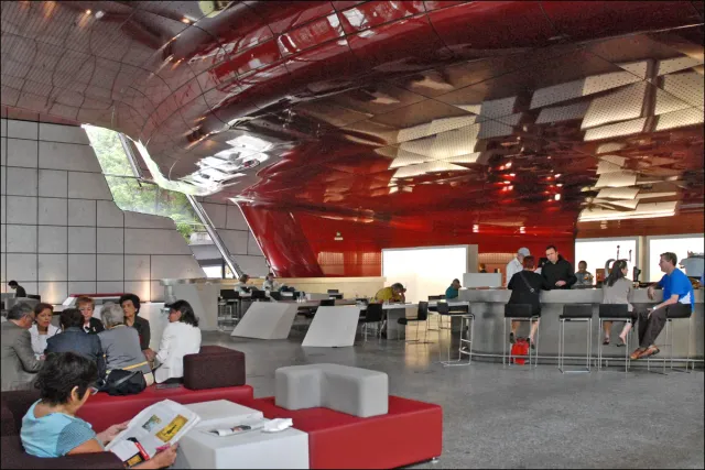 A modern space with a wavy red ceiling above a counter and a seating area with visitors