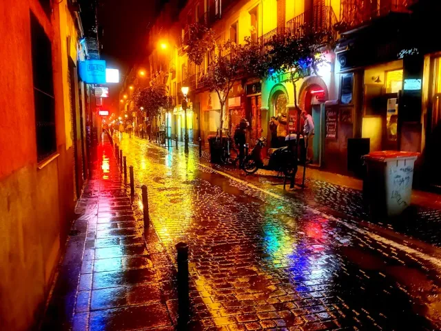A wet cobbled street at night, with colourful neon sign reflections on the stones