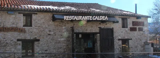 A stone building with a tiled roof and a sign above the entrance, and a little snow on the roof