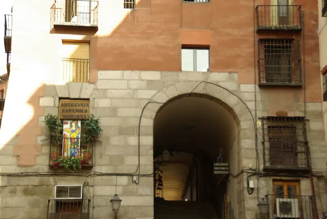 A tall stone arch set into a residential building, with steps descending to a narrow street