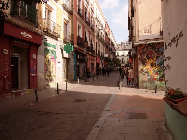 A paved neighbourhood street with colourful murals, small shops and hanging signs