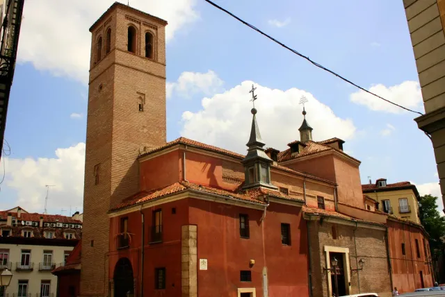 A brick church with a square Mudejar tower and a small dome against a blue sky