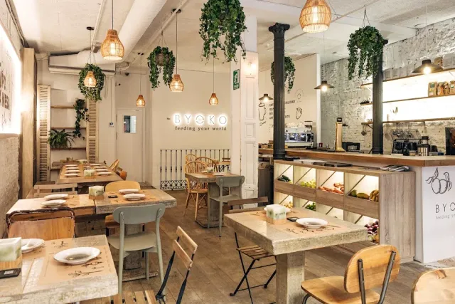 A bright space with hanging plants, wicker lamps and set wooden tables