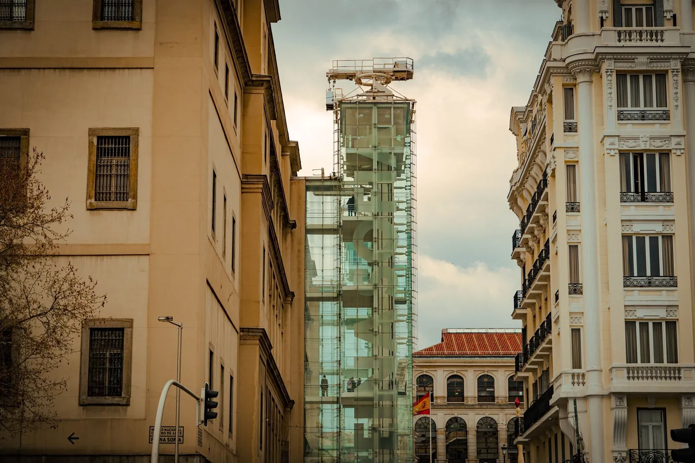A row of townhouses along a Madrid street, with a modern glass elevator tower under scaffolding, Spain