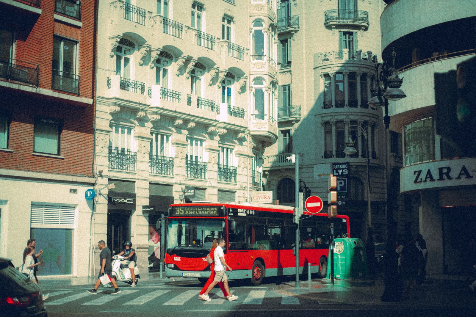 A city bus passing shopfronts on a street in central Madrid in daylight